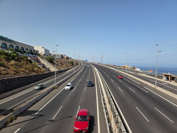 Large autoroute à Tenerife vue depuis une passerelle, avec plusieurs voitures en circulation et la mer au loin.