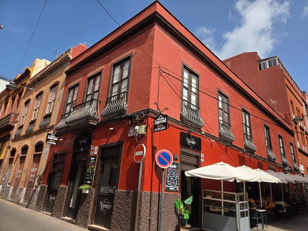 Bâtiment historique rouge à Santa Cruz de Tenerife avec des balcons en fer forgé et un bar à l’angle.