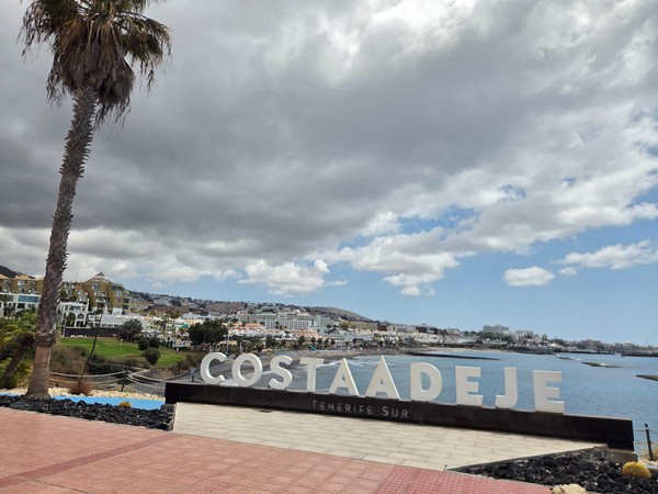 Enseigne de Costa Adeje Tenerife Sur face à la mer, avec des hôtels et des bâtiments touristiques en arrière-plan.