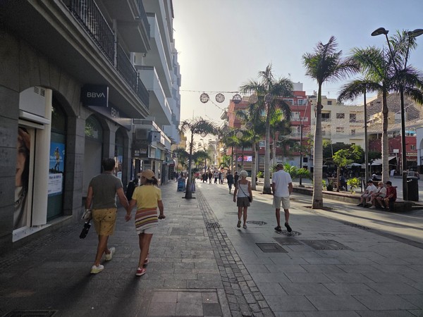 Rue piétonne de Costa Adeje avec des palmiers, des commerces et des touristes qui se promènent en fin d’après-midi.