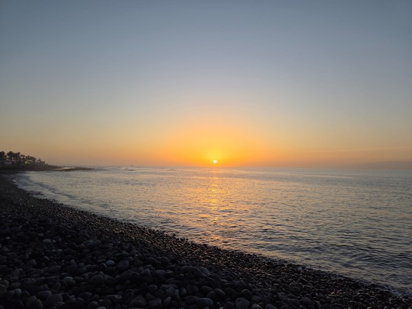Coucher de soleil sur la mer à Costa Adeje avec une plage de galets au premier plan et le soleil à l’horizon.