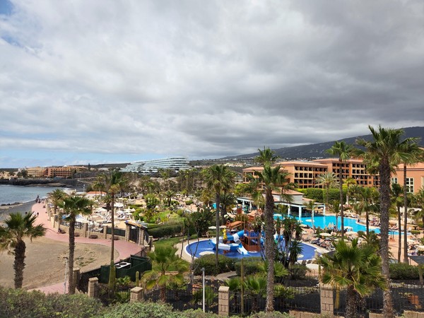 Vue en hauteur d’un complexe hôtelier avec piscines à Costa Adeje, au bord de la côte et entouré de palmiers.