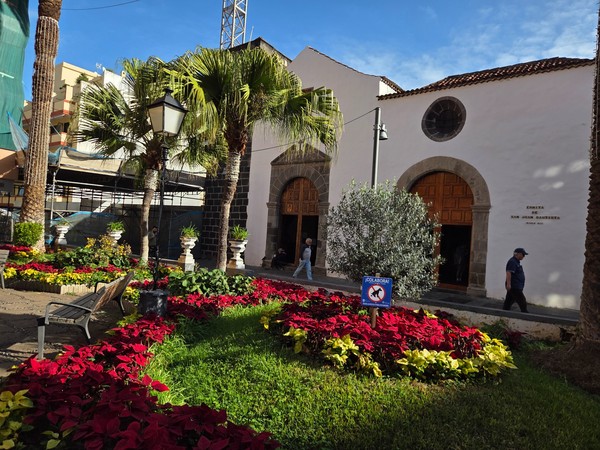 L'ermitage de San Juan Bautista avec sa façade blanche, ses palmiers et un jardin fleuri au premier plan.