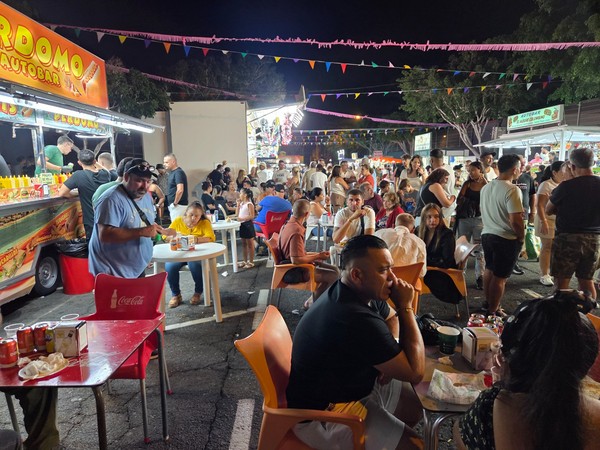 Ambiance nocturne d'une fête locale avec des stands de nourriture, des tables et une foule nombreuse.