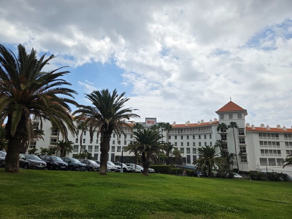 RIU Costa Adeje Le grand bâtiment blanc de l'hôtel RIU Costa Adeje vu depuis une pelouse avec des palmiers.