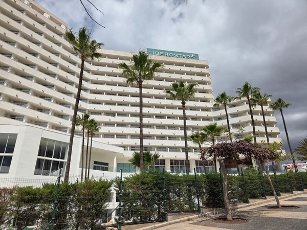 Iberostar Costa Adeje Façade blanche de l'hôtel Iberostar à Costa Adeje avec plusieurs étages de balcons et des palmiers devant.