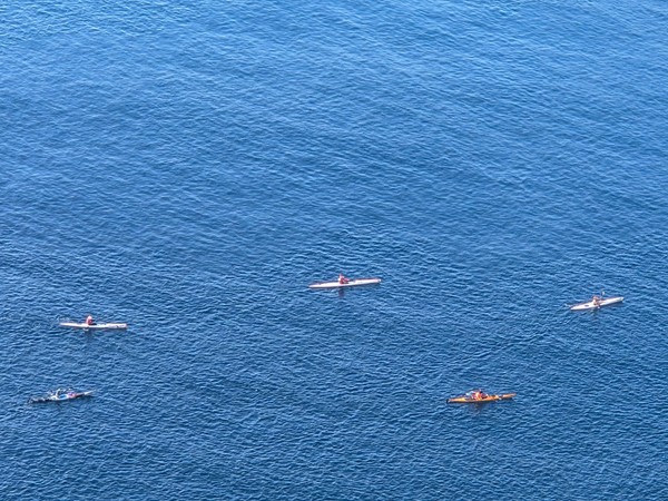 Plusieurs kayaks colorés avancent sur une mer bleue calme, vus depuis un point élevé.