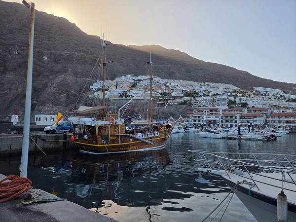 Bateau en bois amarré dans le port de Los Gigantes avec les immeubles blancs sur la montagne en arrière-plan.