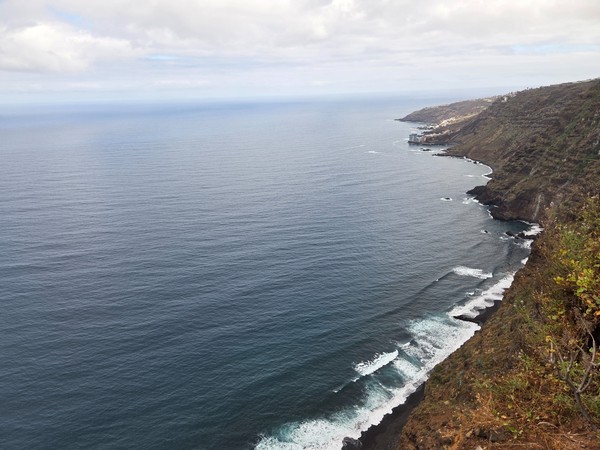 Falaises de la côte de La Garañona avec mer agitée, rochers volcaniques et immeubles au sommet.