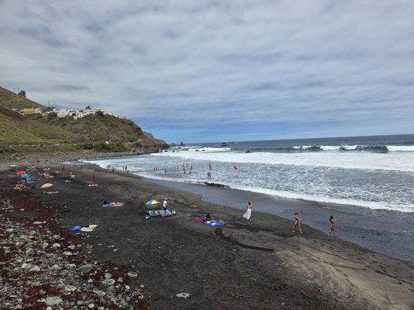 Plage d’Almáciga Vue de la plage d’Almáciga à Tenerife, avec son sable noir, des baigneurs, l’océan agité et les maisons du village sur la falaise.