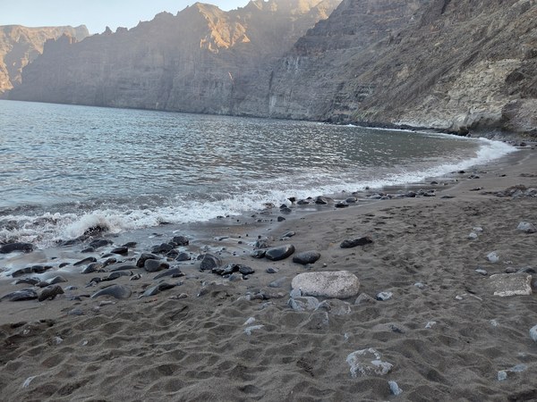 Plage de Los Guíos à Tenerife, avec sable sombre, eau calme et les impressionnantes falaises de Los Gigantes.