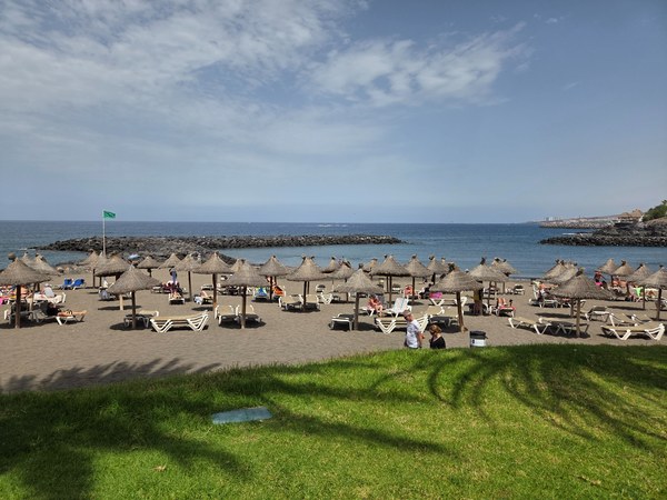 Playa El Bobo Playa El Bobo à Tenerife, avec sable doré, parasols en paille, transats et une mer calme dans une petite baie.