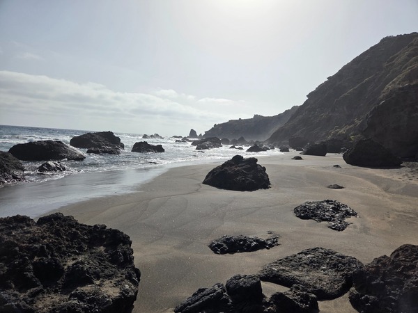 Plage de Las Breñas Petite plage rocheuse de sable sombre avec gros rochers volcaniques et lumière vive sur la côte.