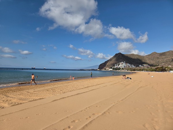 Grande plage dorée de Las Teresitas avec montagne, mer calme et quelques promeneurs sur le sable.