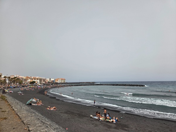 Vue sur la plage noire du Puertito de Güímar avec ville côtière, digue et baigneurs dispersés.