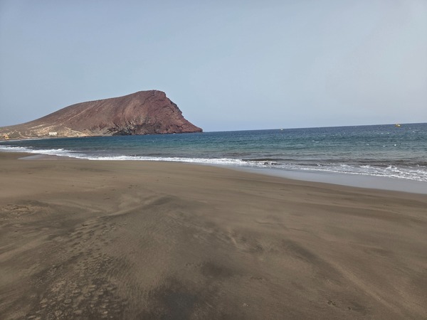 Playa de La Tejita avec vaste sable sombre, mer ouverte et la montagne rouge en toile de fond.