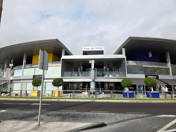 Façade moderne de Plaza del Duque avec boutiques, architecture contemporaine et ciel gris.