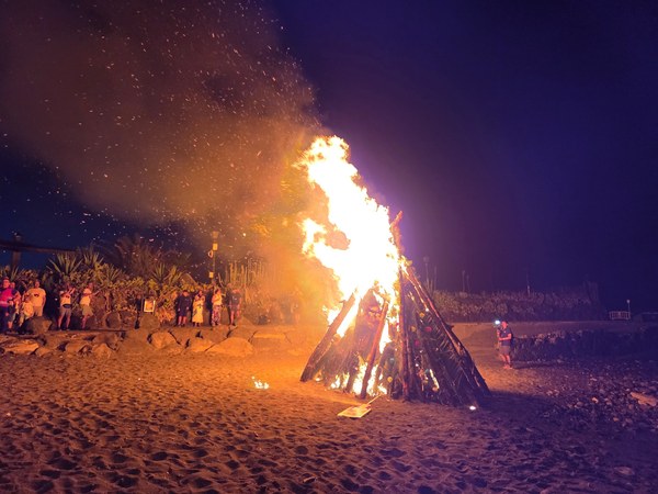 Grand bûcher en flammes sur la plage pendant la nuit de la Saint-Jean à Tenerife, entouré de spectateurs.