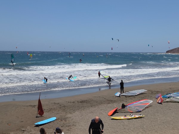 Plage d’El Médano avec véliplanchistes, kitesurfeurs et vagues sous un ciel dégagé à Tenerife.