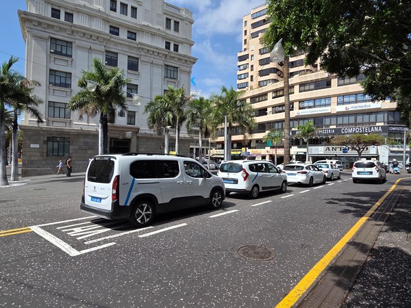 Rue de Santa Cruz de Tenerife avec taxis blancs, palmiers et immeubles modernes sous un ciel bleu.
